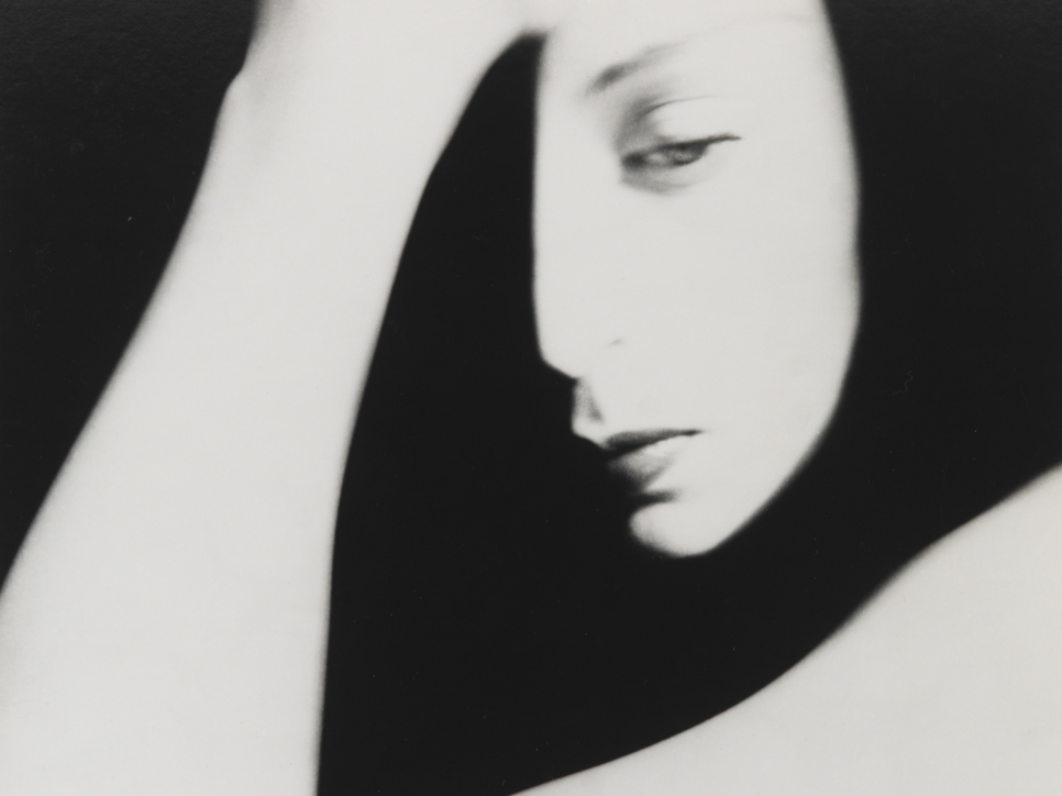 Black and white photographic by Bill Brandt featuring a shadowed close-up view of half of a woman's face and her hand resting on her forehead 
