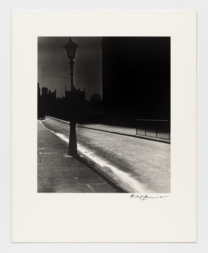 Black and white photographic by Bill Brandt featuring an empty street at night and the silhouette of a street lamp